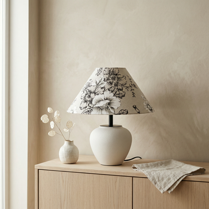 Minimalist japandi ceramic table lamp with white rounded base and a flower linen lampshade on a light wood console