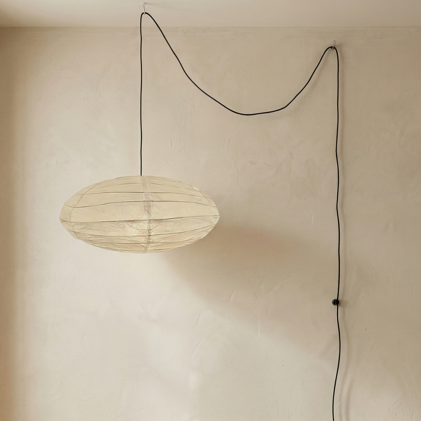 An oval-shaped, minimalist paper pendant light fixture hanging from a simple black cord, showcasing a delicate rice paper lantern design.