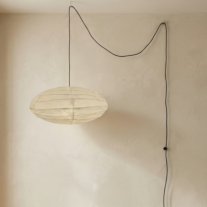 An oval-shaped, minimalist paper pendant light fixture hanging from a simple black cord, showcasing a delicate rice paper lantern design.