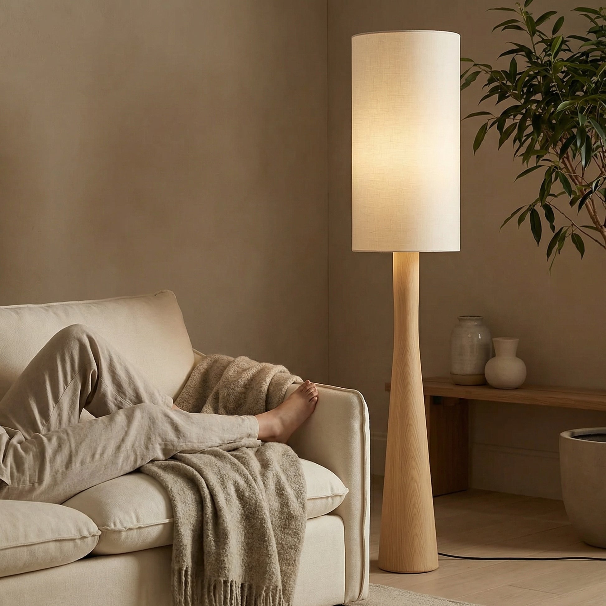 Lifestyle shot of a modern tapered floor lamp creating a cozy, ambient reading nook in a neutral-toned living room.