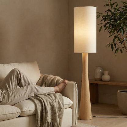 Lifestyle shot of a modern tapered floor lamp creating a cozy, ambient reading nook in a neutral-toned living room.